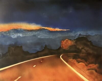 A highway at night with headlights reflecting roadsides with the remaining light in the sky illuminating a rock formation in the distance.